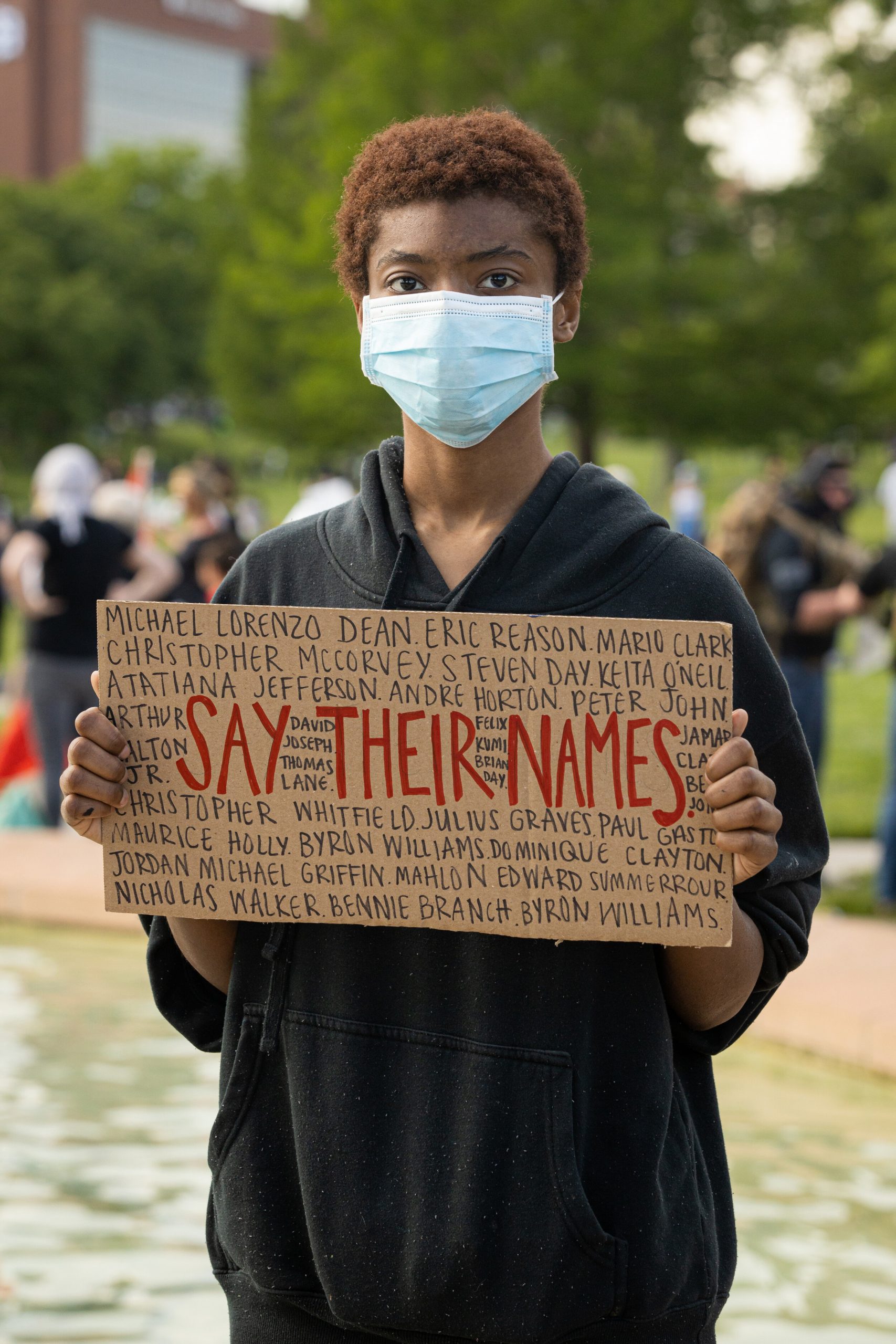 young man hold poster reading "Say their names"