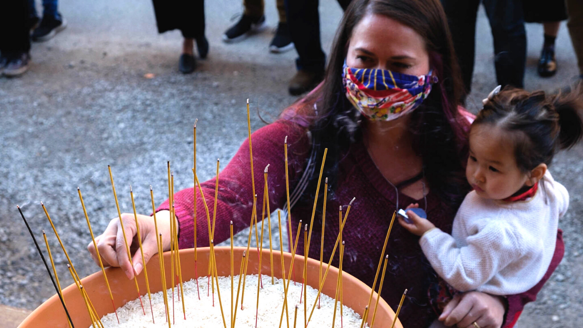 Kearsha Xu and Astra Xu, wife and daughter of Kansas Rep. Rui Xu, place an incense stick in a pot filled with rice, as part of a Vietnamese tradition during the Stop Asian Hate vigil on March 28.
