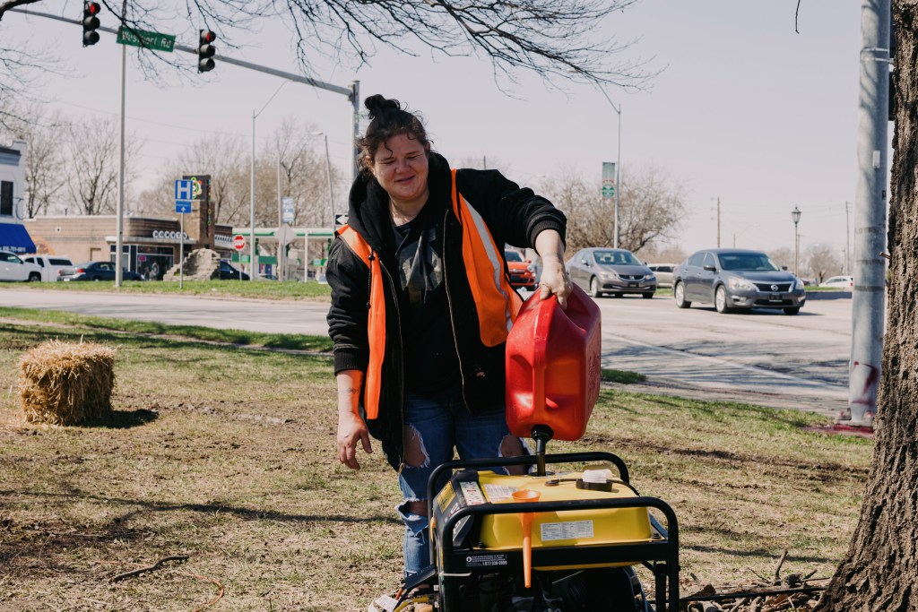 Ashley Handy pours gasoline to power a generator at Camp 6ixx in the Westport area of Kansas City. The camp formed this winter and has received a notice to vacate from the city. 