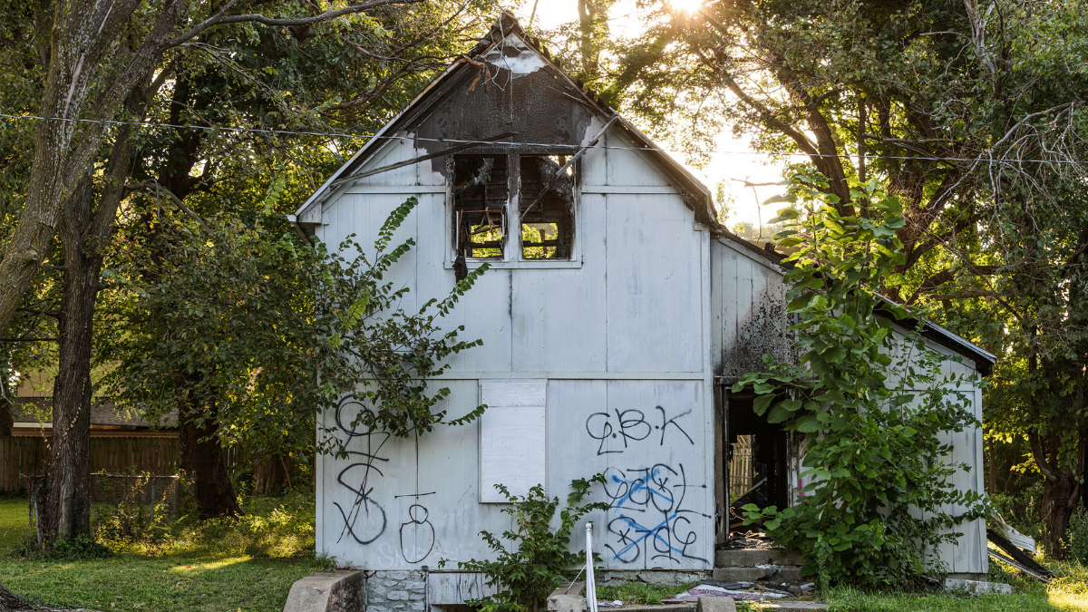 The burned and abandoned property at 2415 Kensington Ave. in Kansas City, MO has graffiti covering the property. Much of the roof is missing or scorched, and fire damage can be seen throughout the home.