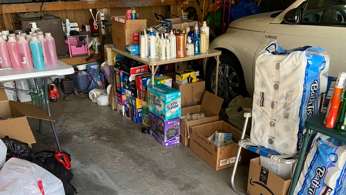 Photo shows cleaning supplies piled onto two tables inside of a garage.
