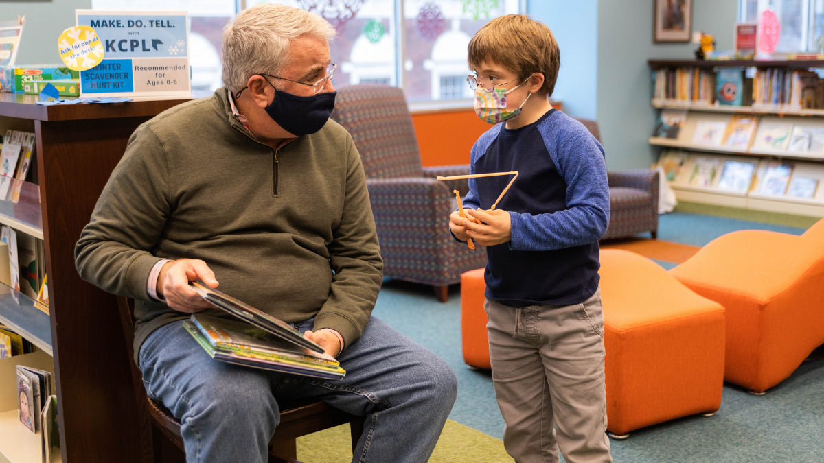 Mark Coleman, left, holds a stack of books that his son, Drew, has chosen to check out from the Central Branch of the Kansas City Public Library over break. Drew has Down syndrome and receives special education services through his school.