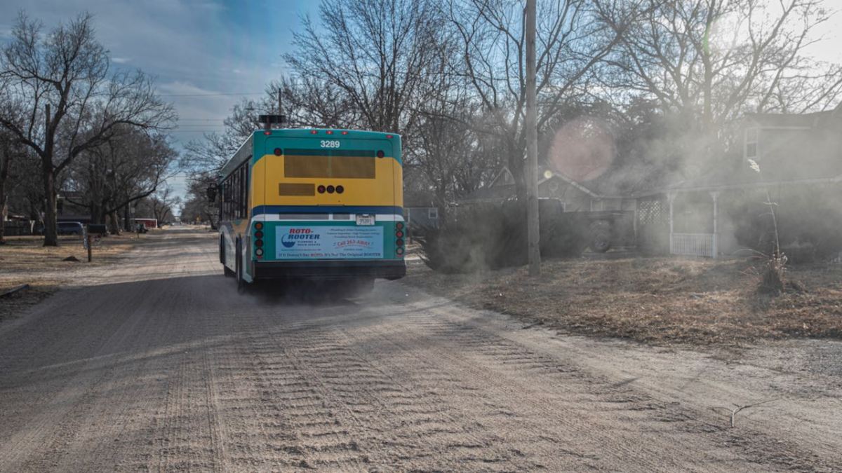 A city bus drives down an unpaved road in Orchard Breeze, a neighborhood with unpaved streets just west of downtown Wichita. Property owners can petition the city to pave their roads if they’re able to pay. (Fernando Salazar/The Beacon)