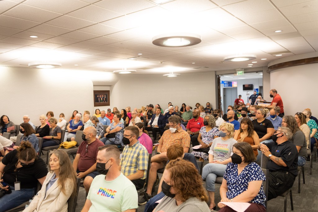 People sit in rows of chairs, filling a room.