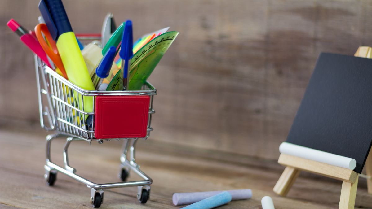 A tiny shopping cart filled with school supplies next to a tiny blackboard
