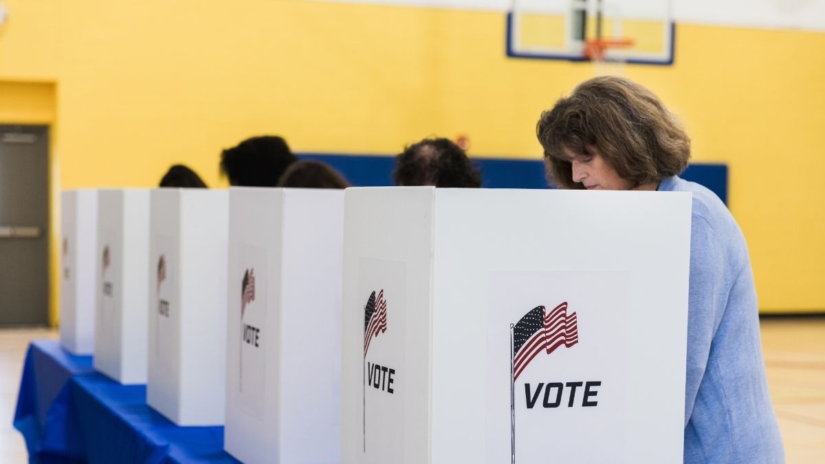 a woman appears to vote at a row of white voting booths along a yellow wall