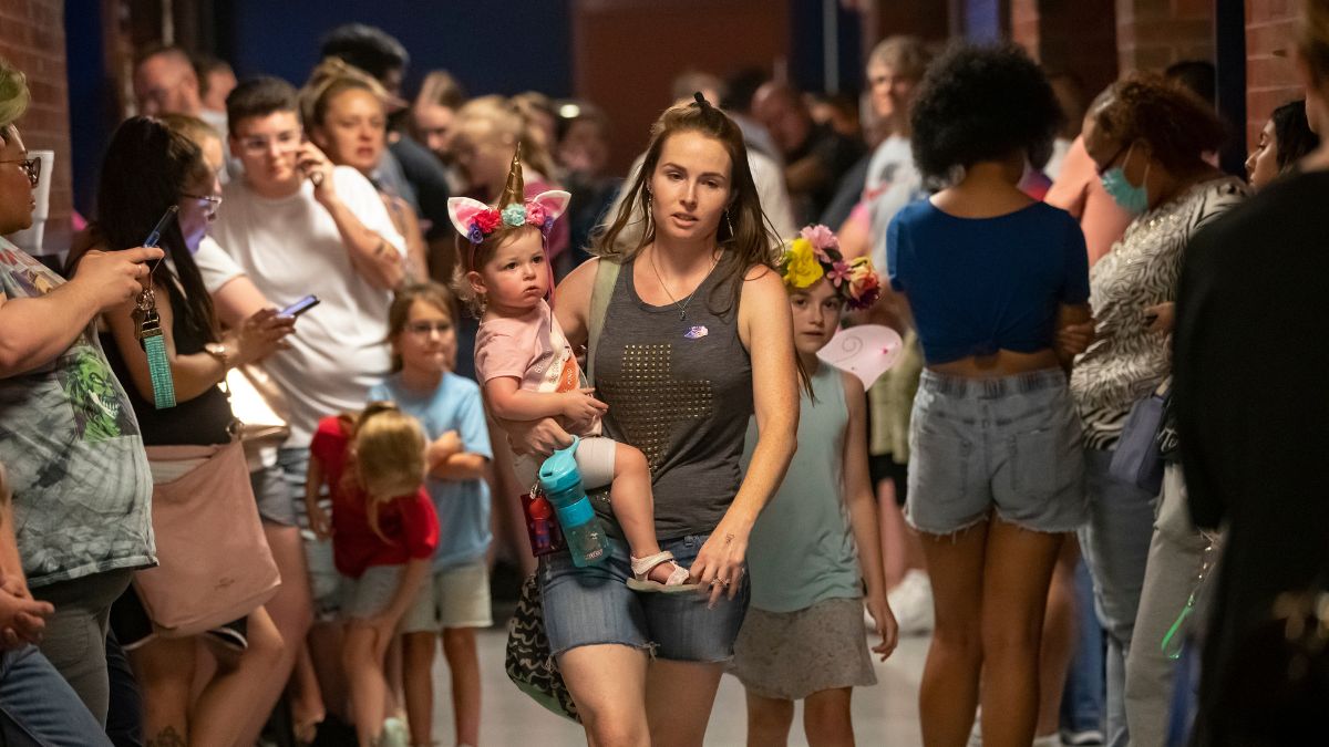 A woman holding a child on her hip walks through a large crowd of people waiting in line amid high voter turnout in Wichita