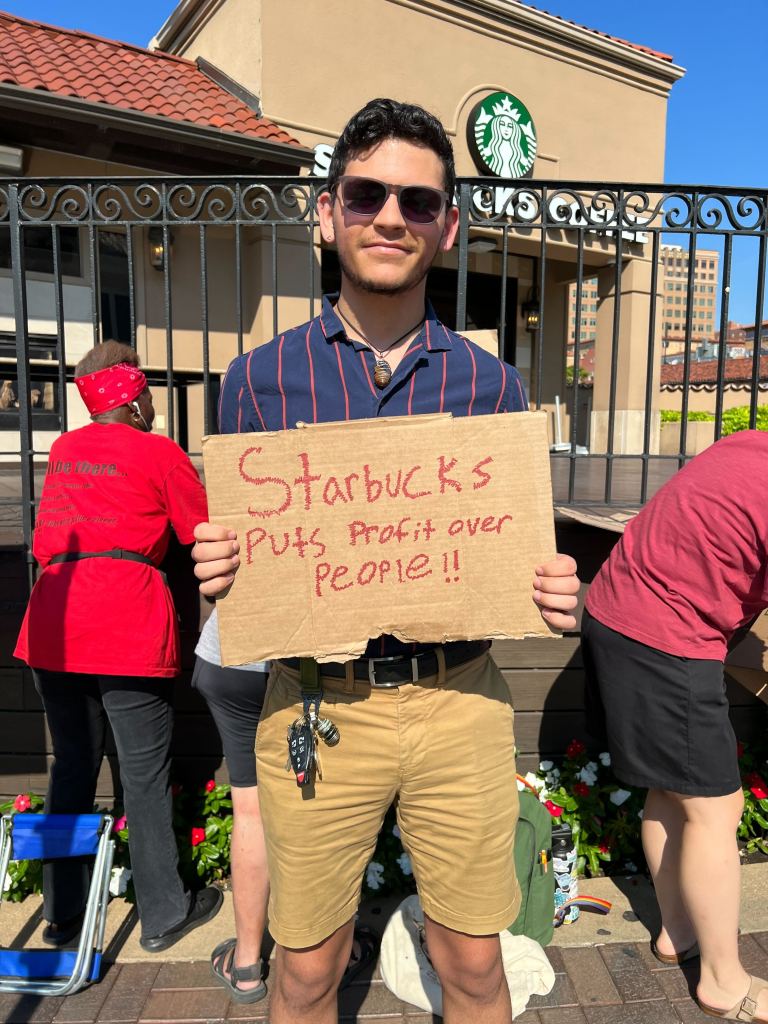 Man stands in front of Starbucks with a sign that reads "Starbucks puts profit over people!!"