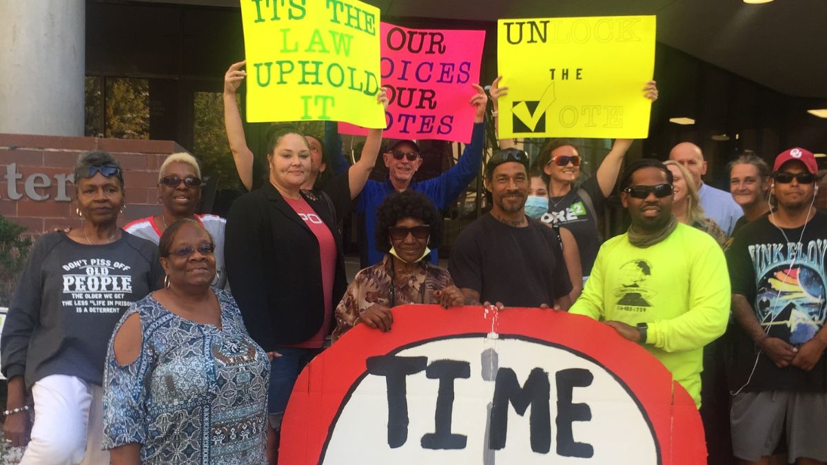 15 demonstrators at the Jackson County jail, holding signs that say, "It's the Law. Uphold it," "Unlock the Vote" and "Time for Justice."