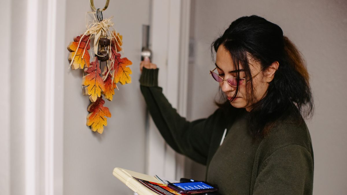A canvasser knocks on a white door decorated with an autumn wreath.