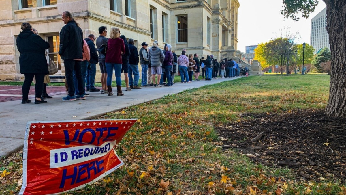 Voters stand in line with a vote here sign in front of them.