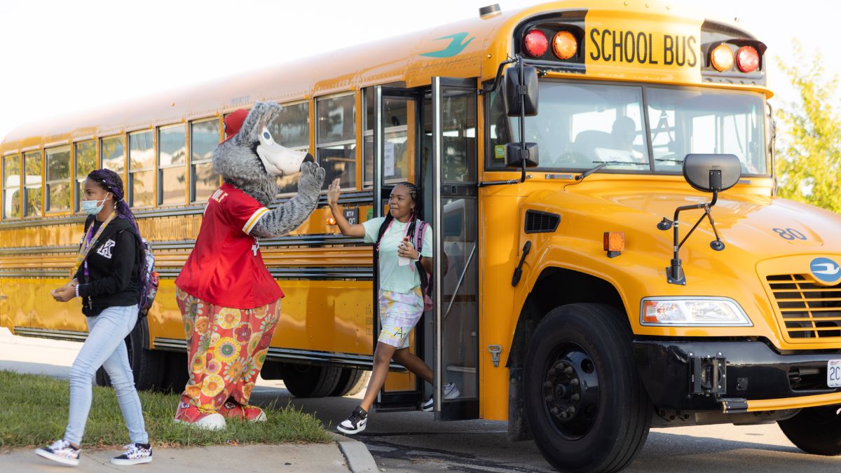 A student high fives a wolf mascot while exiting a bus