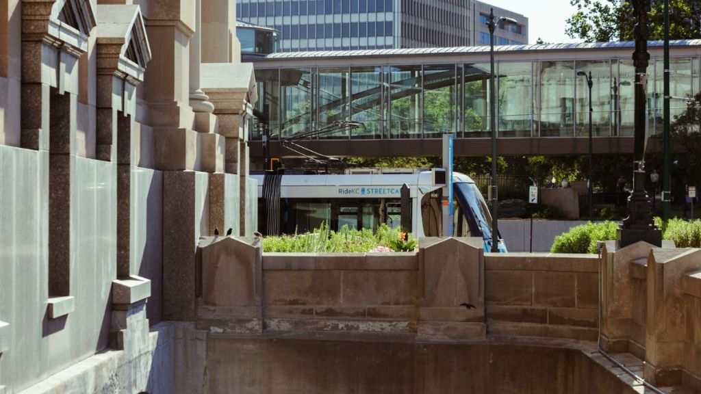 The RideKC streetcar moves along Main Street, passing behind Union Station. A Crown Center pedestrian bridge is visible in the background.