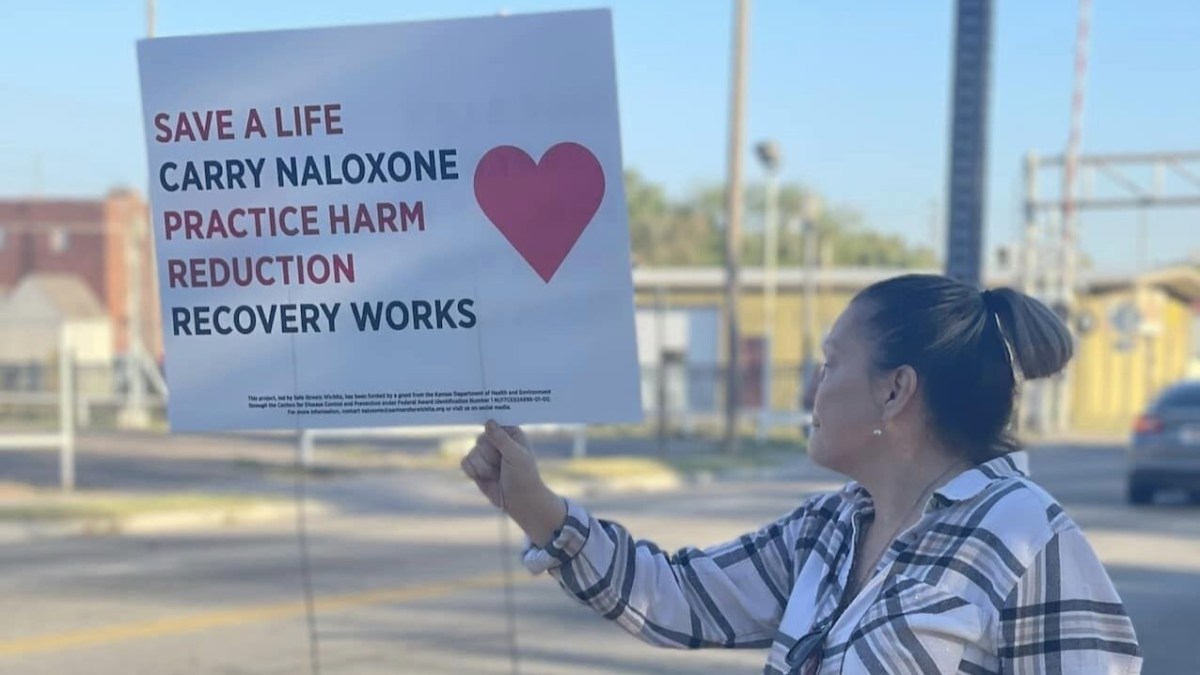 A woman holds up a sign directing people to use Narcan.