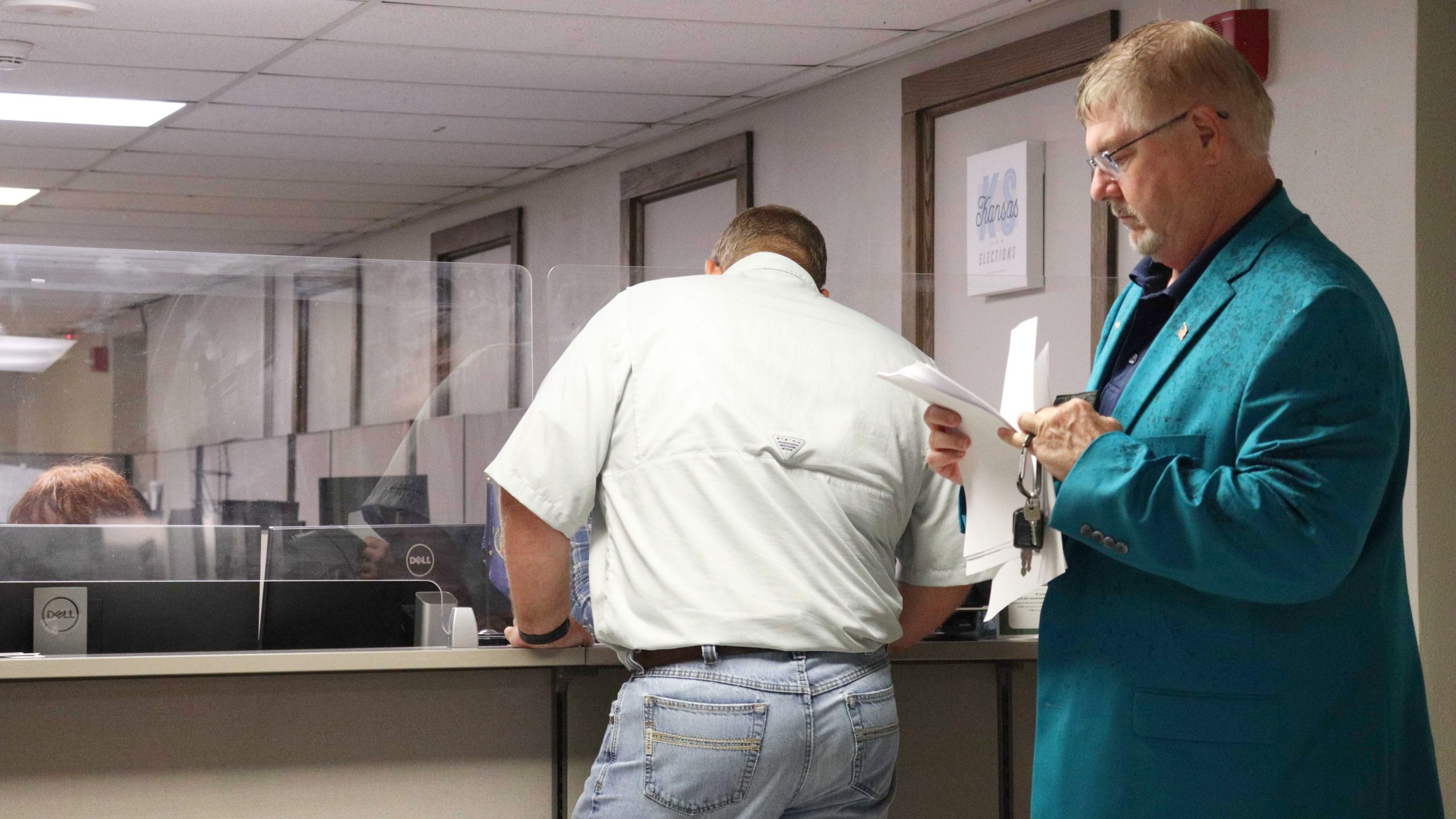 Two men stand in front of a desk at the Sedgwick County Election's Office.