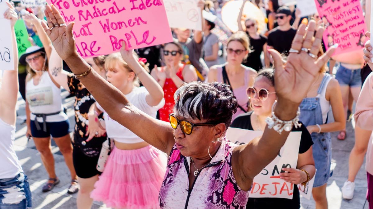 A woman stands in the center of the shot with her arms outstretched amid a protest over Missouri's abortion ban.