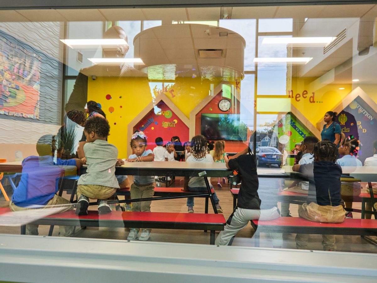 Schoolkids sitting at tables seen through a window with a reflection of a man.