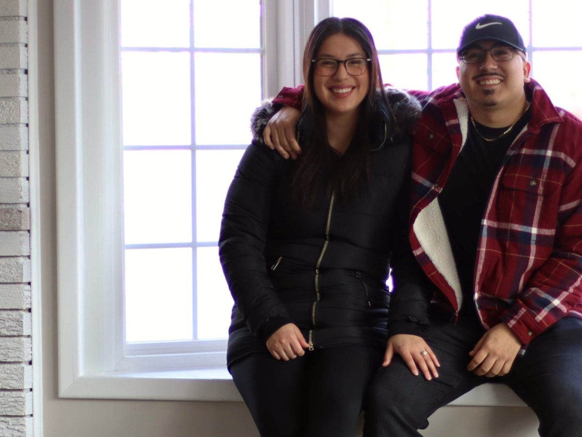 Carla Mendez and Jacob Salas sit in the window of their newly bought home. His arm is wrapped around her. The house is still empty.