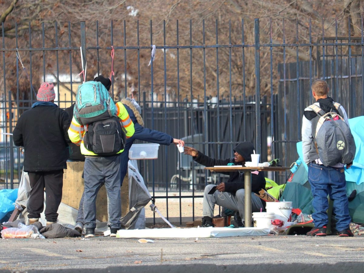 Four unhoused people sit at their camp.