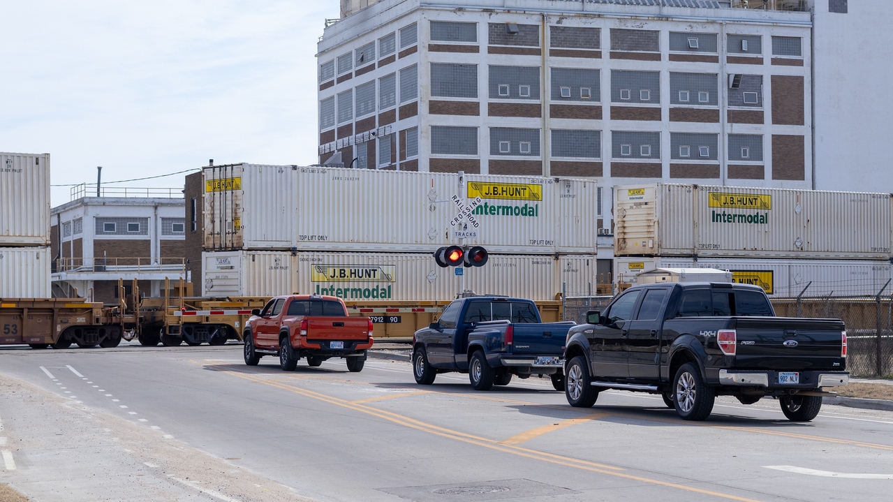 Three cars sit waiting for a train to pass.