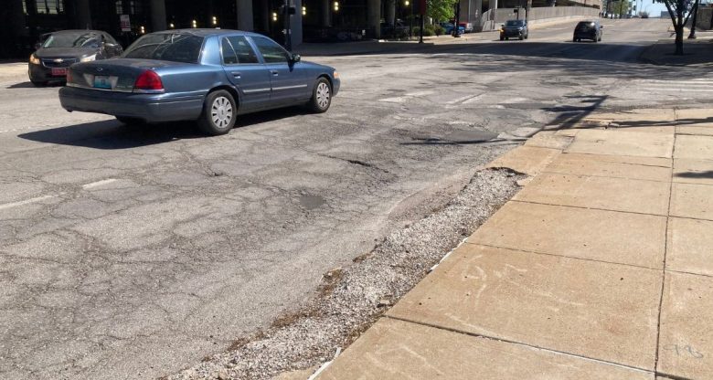 Cars driving down Broadway Boulevard, next to the convention center, with a large pothole in the road.