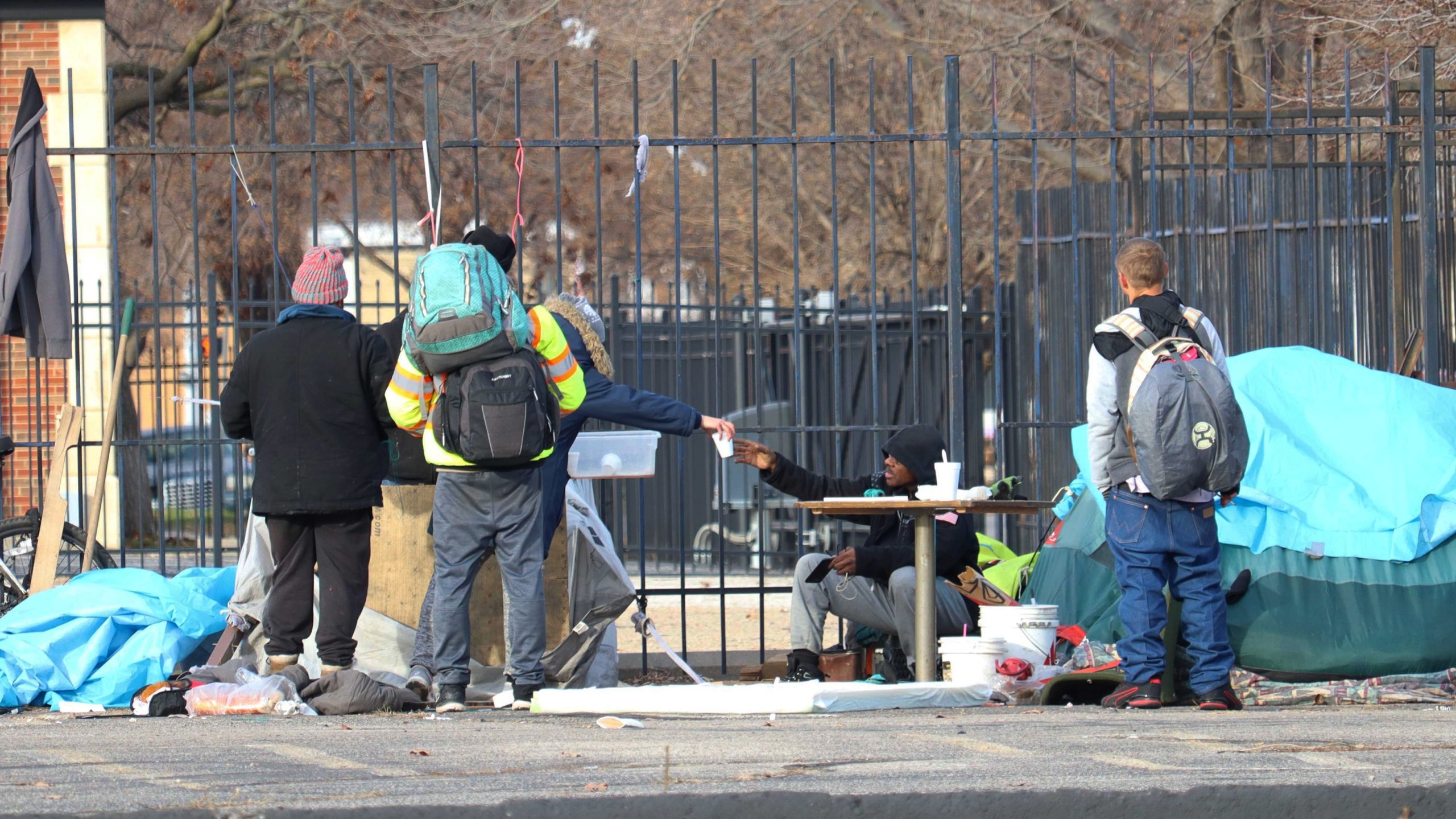 Four unhoused people sit at their camp.