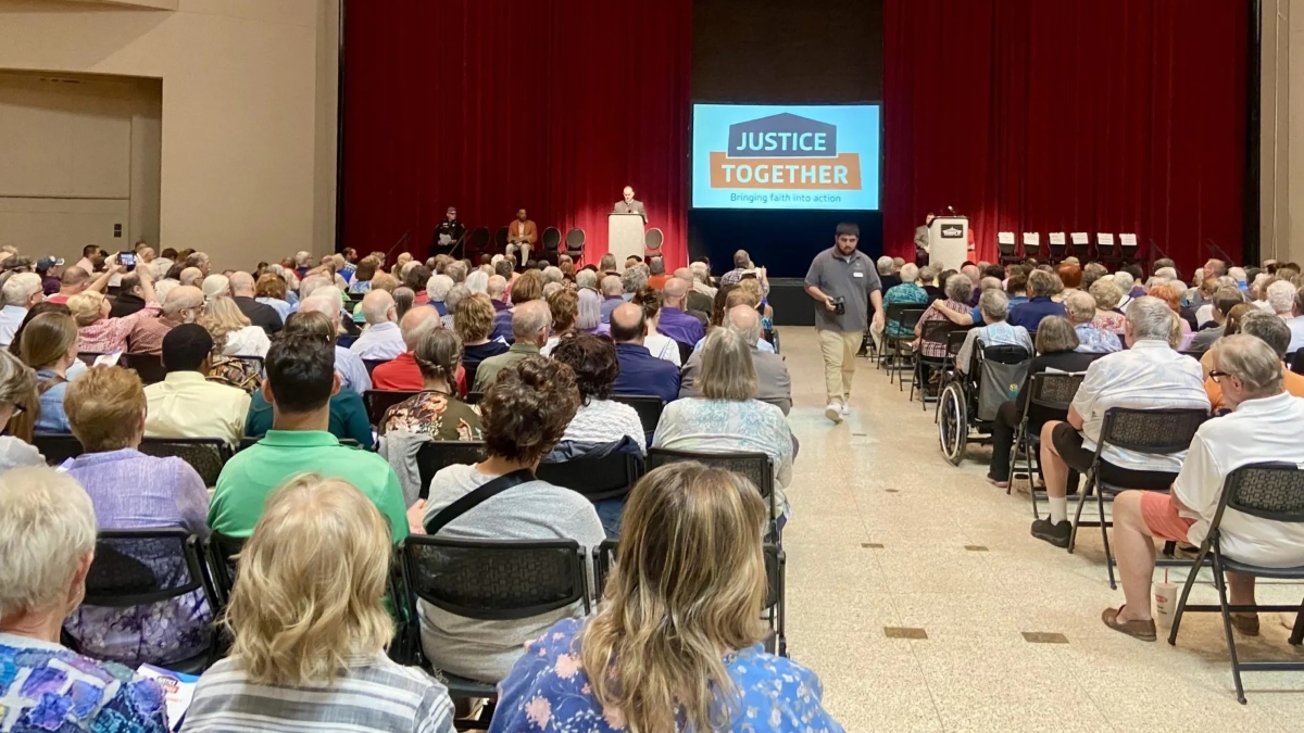 people sit in folding chair, on a screen at the front are the words justice works. municipal ID