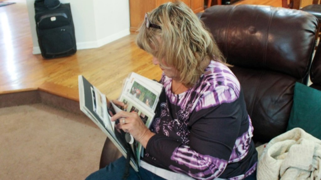 woman with blonde hair and a purple top sits in a leather recliner and looks at photos.