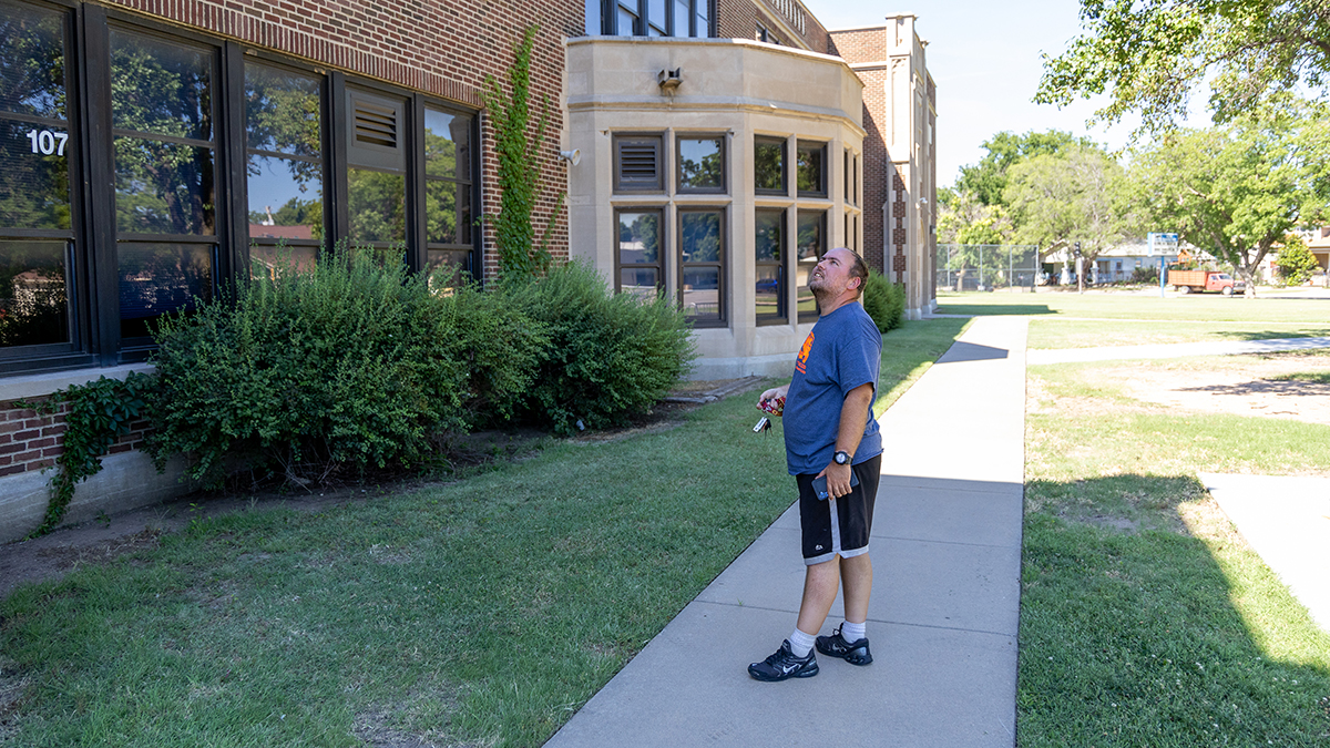 A man looks at a school building with a confused expression.