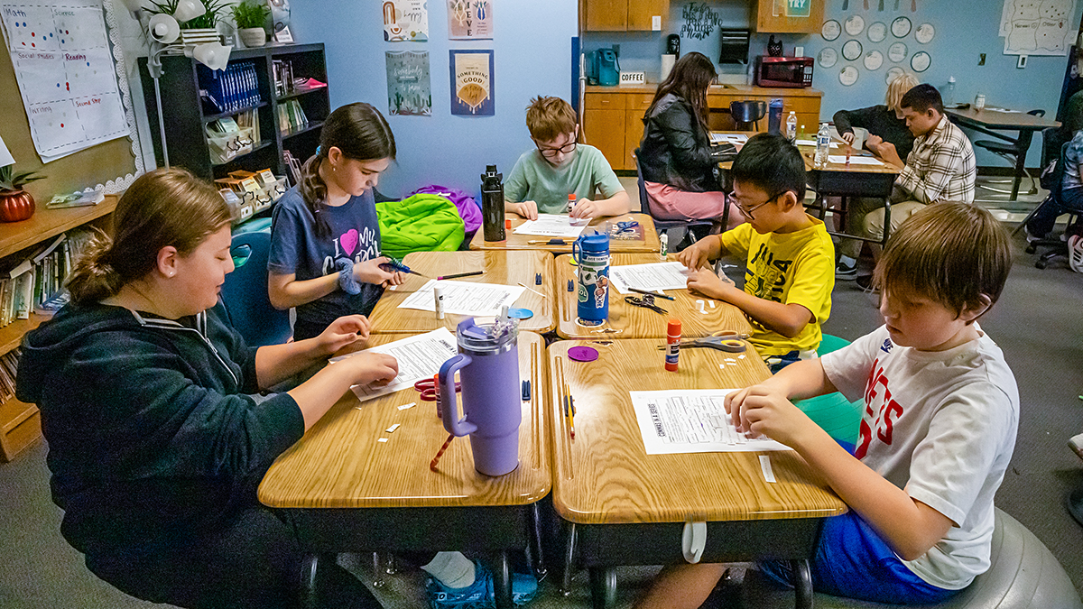 Children gather around a table to use school supplies.