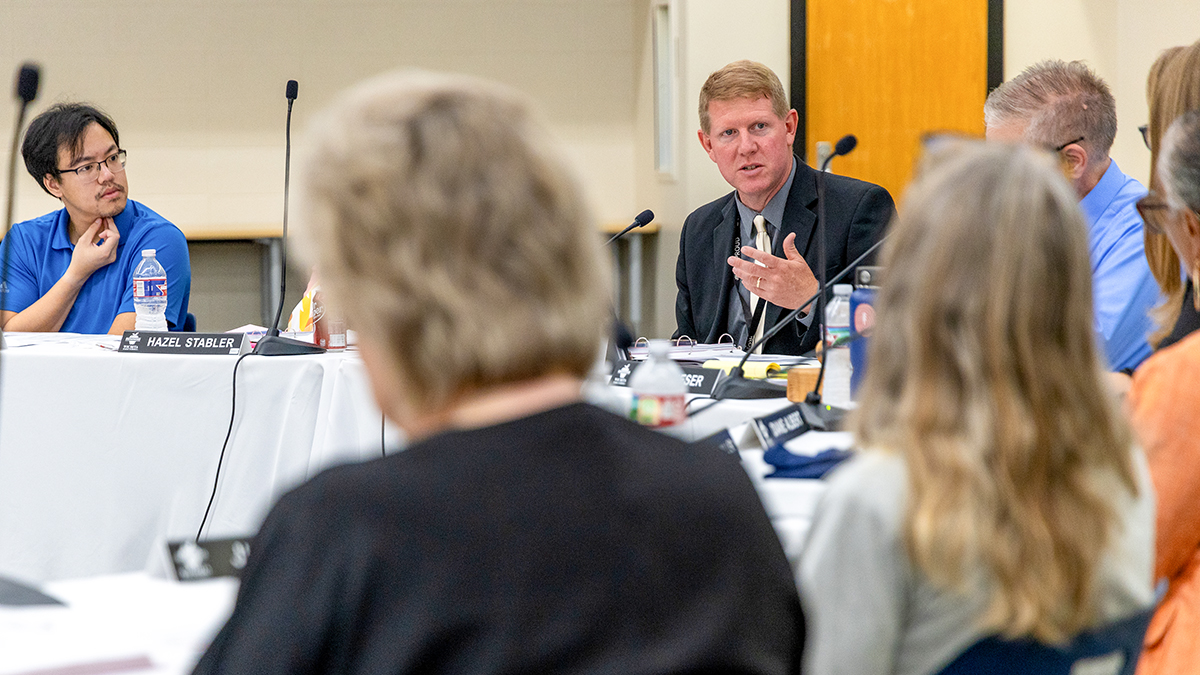 A man speaks with colleagues during a school board meeting.