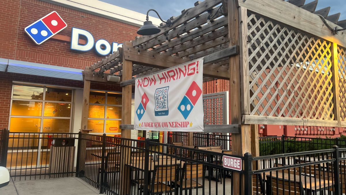 A sign at Domino's reads Now Hiring Under New Leadership. There is a QR code on the sign.