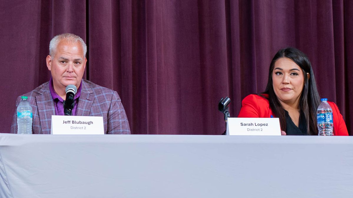 Jeff Blubaugh sits on the left of a table on a stage holding a microphone. Sarah Lopez sits at the table on the right. Both are running for the Sedgwick County Commission District 2 seat.