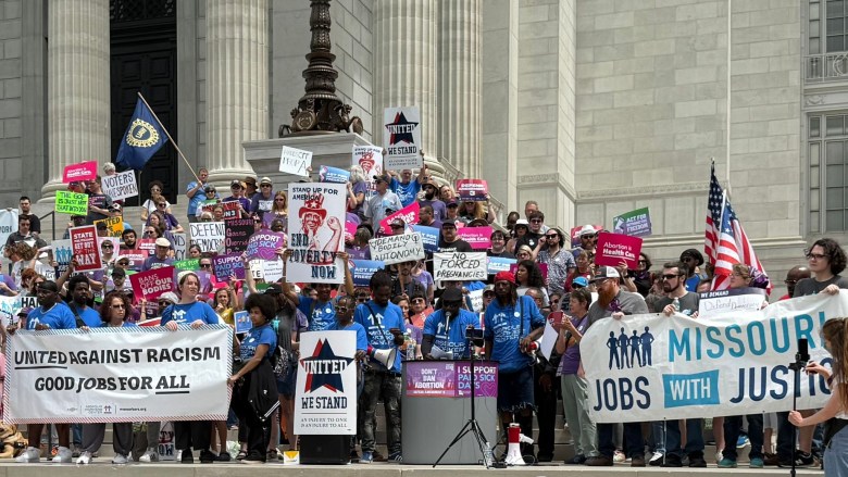 A crowd of labor and abortion advocates stand on the steps of the Missouri Capitol with signs reading "Bans of our bodies" and "United against racism — good jobs for all."