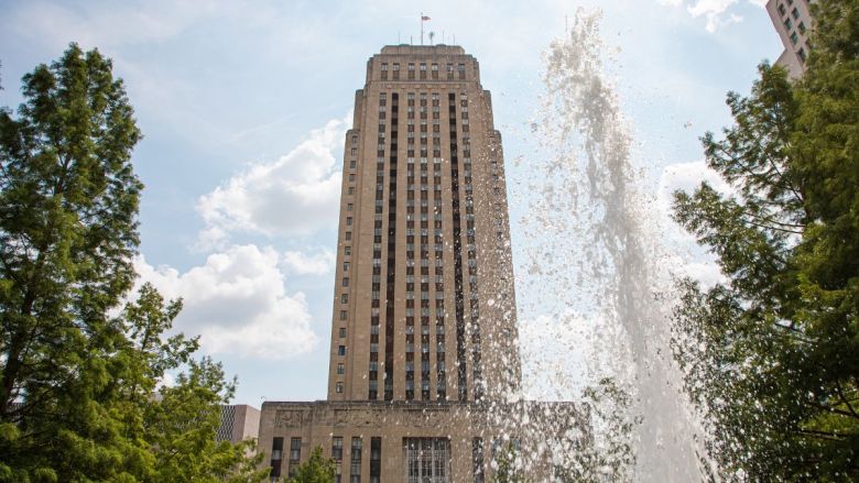 City hall, with a fountain in front of it and two trees on either side.