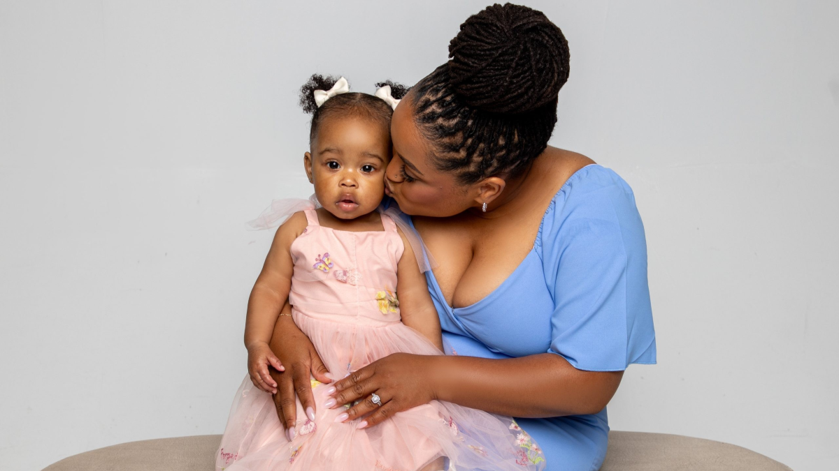 Baby A'ja sits in her mom, Nina's lap on a bench in a photo studio. Nina gives her a peck on the cheek.