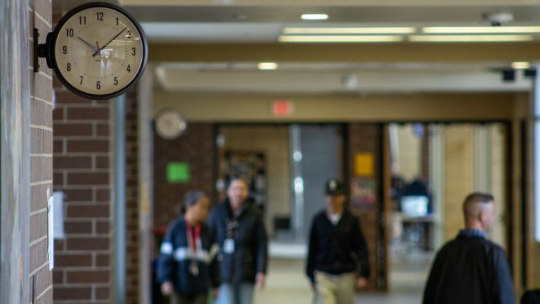 People walking through a school hallway. A clock sits in the upper lefthand corner.