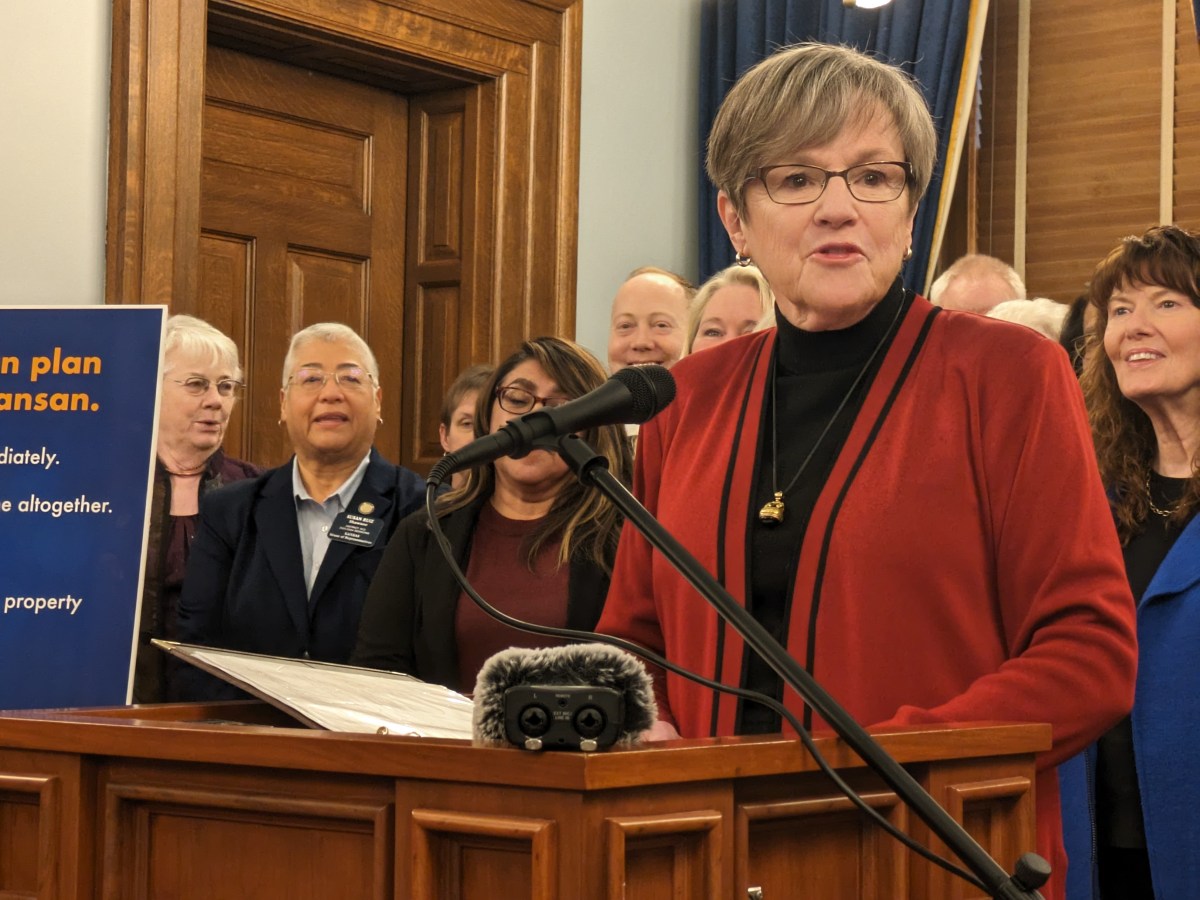 Laura Kelly speaks at a podium in a crowded room