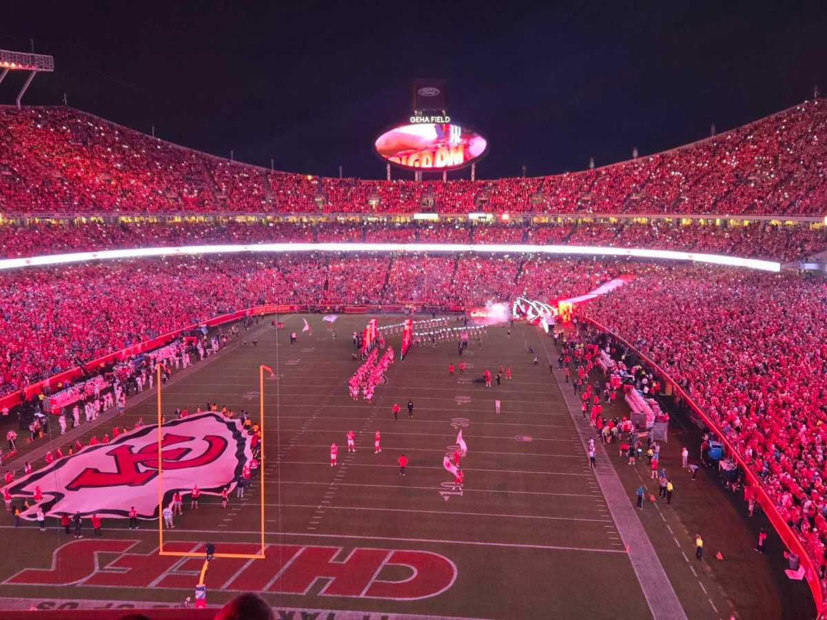 A photo of the inside of Arrowhead Stadium. A flag the shape of the Chiefs logo is on the stadium and all the lights are red.