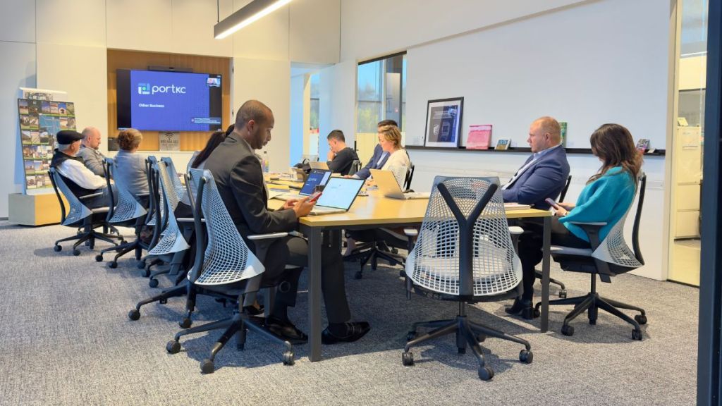 Ten people sit around a table at the Port KC board room at the Berkley Riverfront. A TV screen hangs in the background showing the Zoom meeting.