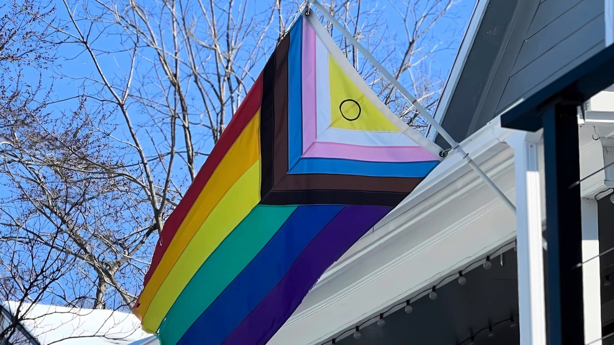 An LGBTQ pride flag is waiving in the wind outside of someone's home.