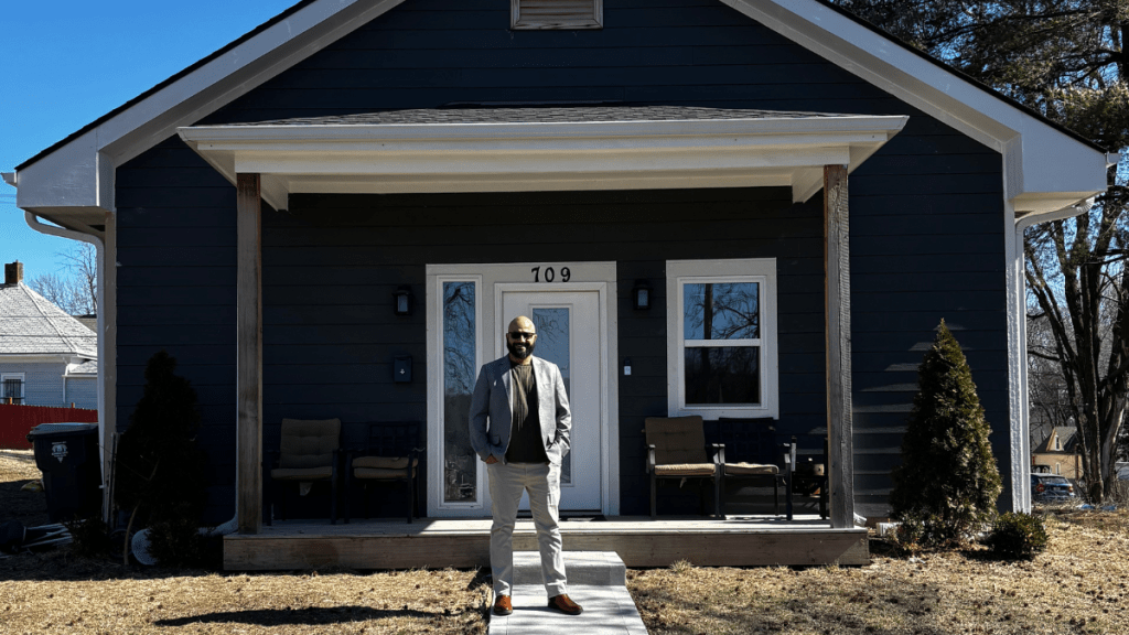 Reda Ibrahim stands on the front walkway of a newly completed dark-blue home in Kansas City’s Lykins neighborhood.