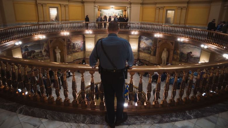 A law enforcement officer stands in the Statehouse looking down at people walking through the halls.