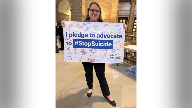 A woman with blonde hair holds a sign pledging to advocate to end suicide.
