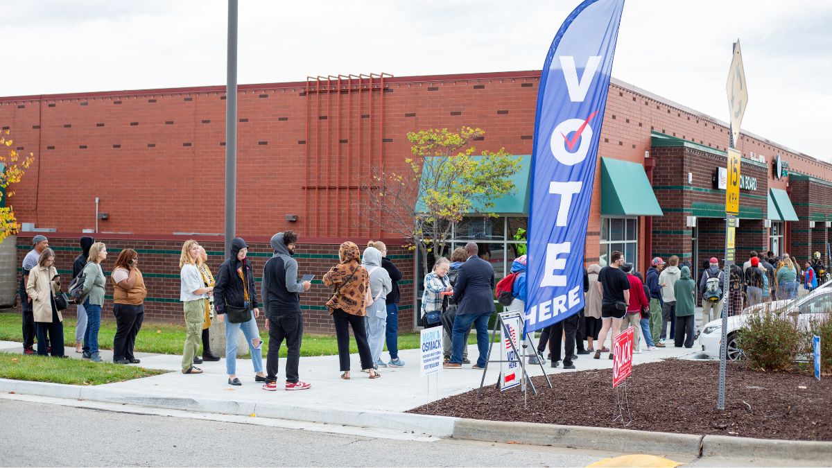 A line of dozens of people outside the brick KC election board office. A blue banner says, "Vote," with a smattering of campaign signs beneath it.