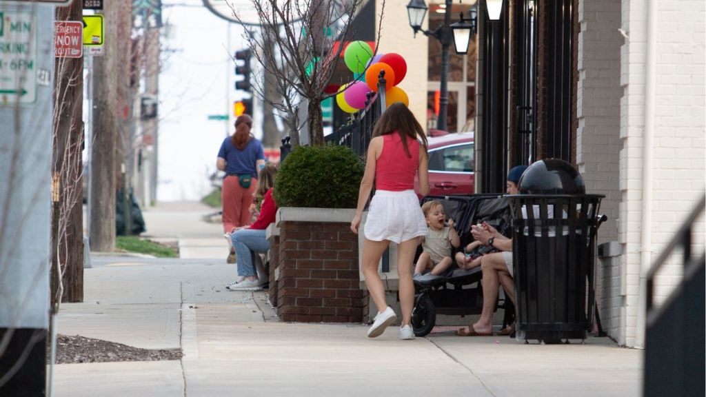 Six people, including two small children, sitting outside of a shop in Brookside. The children appear to be eating ice cream, while others are chatting.