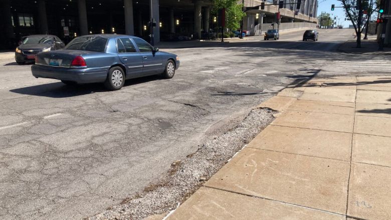 Cars driving down Broadway Boulevard, next to the convention center, with a large pothole in the road.