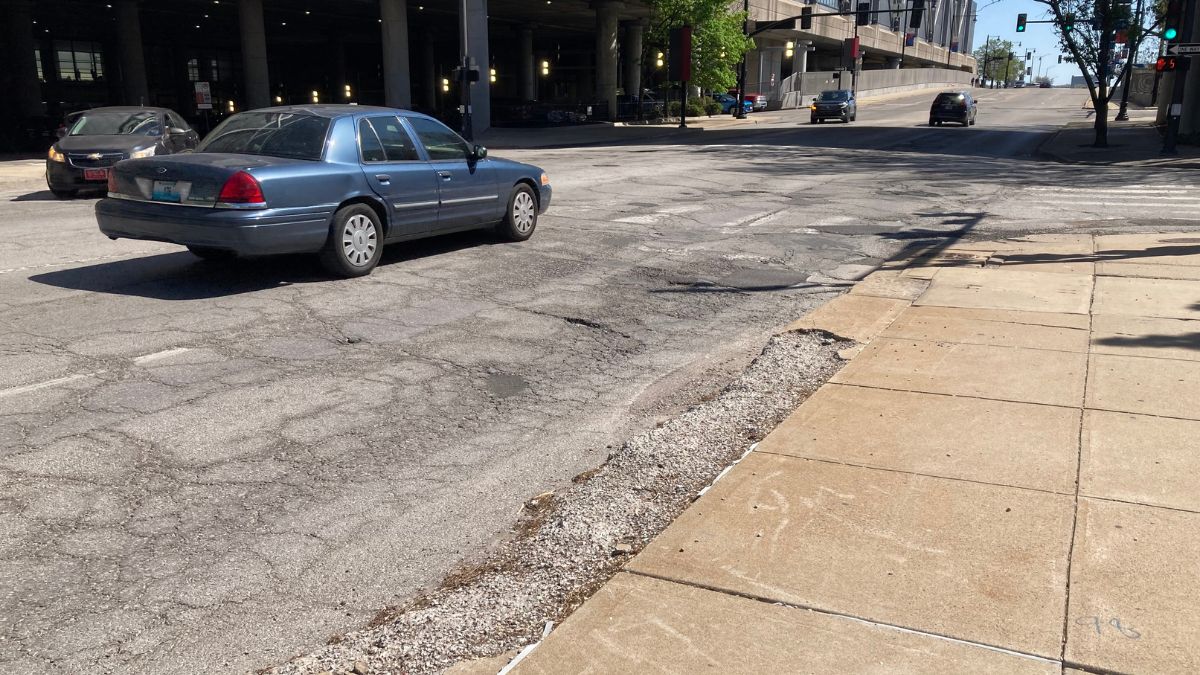 Cars driving down Broadway Boulevard, next to the convention center, with a large pothole in the road.
