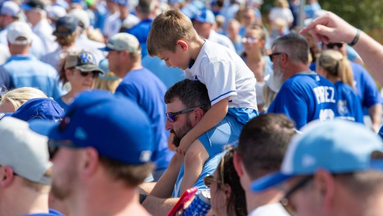 A crowd of Royals fans dressed in blue, with the camera's focus on an adult with a child sitting on their shoulders.