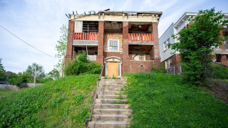 A colonnade apartment building on a hill, with boarded up doors and a collapsing roof